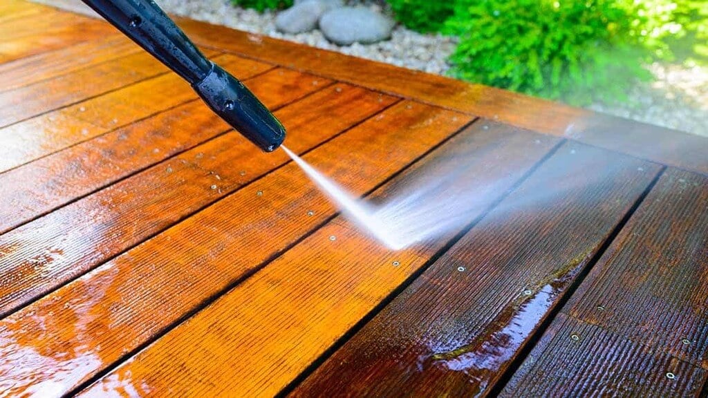 A person spraying water on a wooden deck
