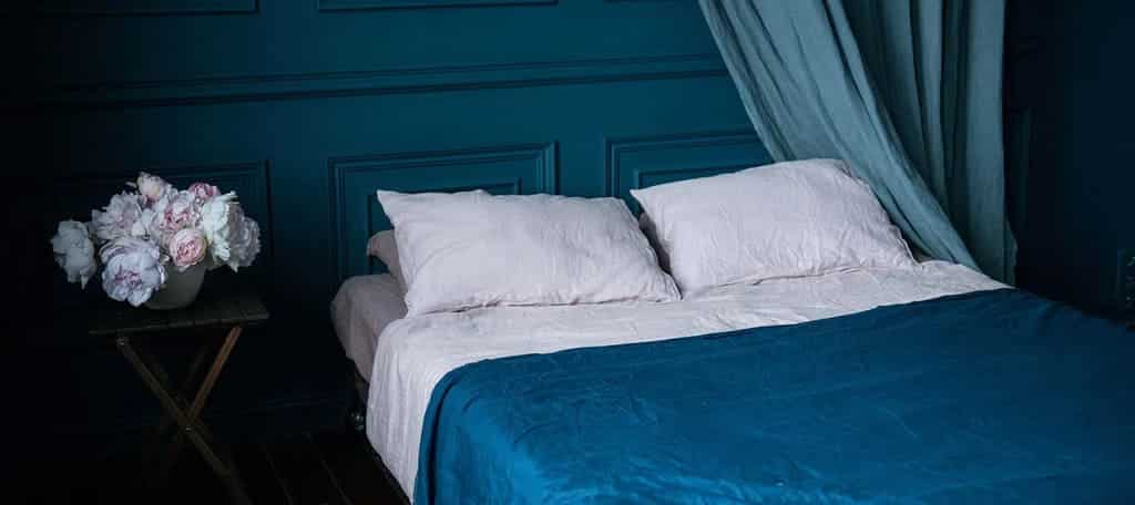 A bed with a blue comforter and white pillows

