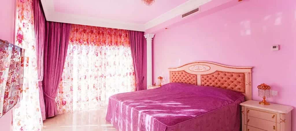 A bedroom with pink walls and curtains and a pink bed
