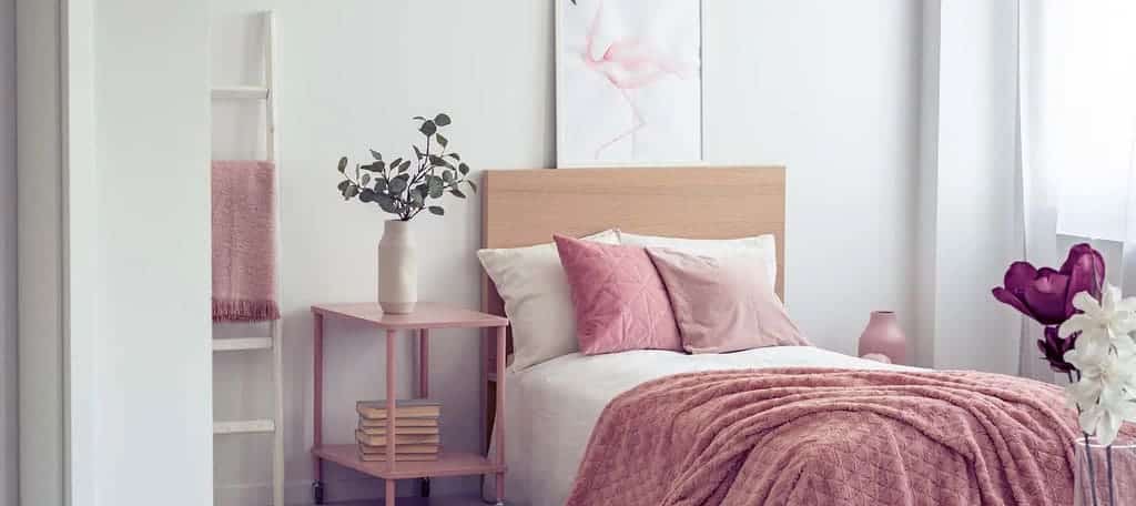 A bedroom with a pink bed and a white wall
