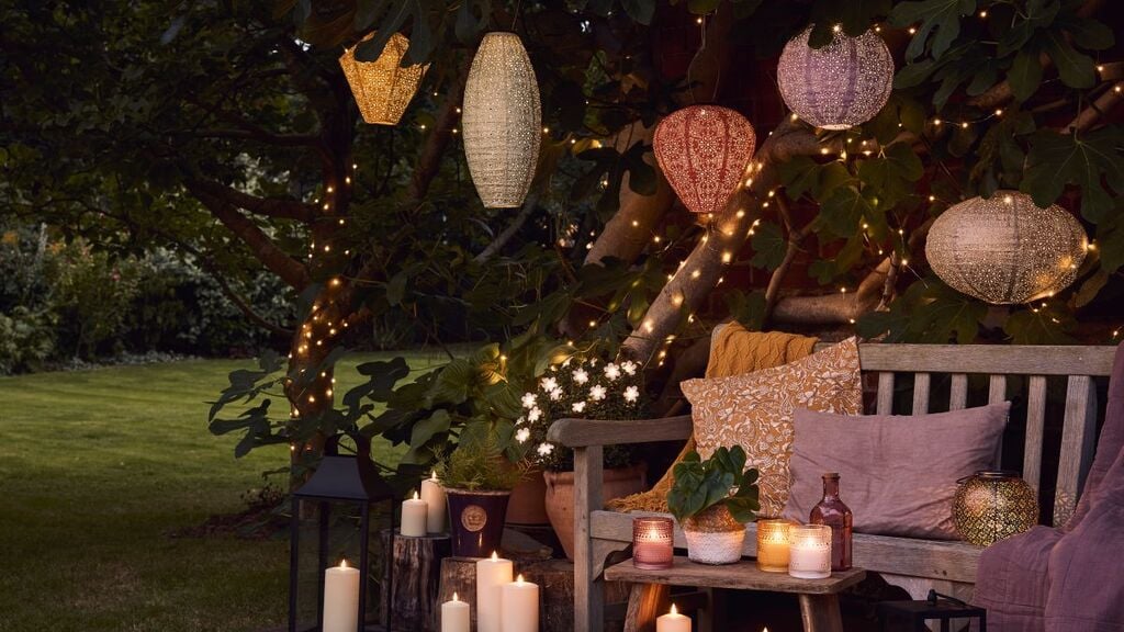 A wooden bench sitting under a tree filled with lit candles
