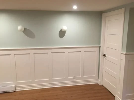 A room with a hard wood floor and white paneling
